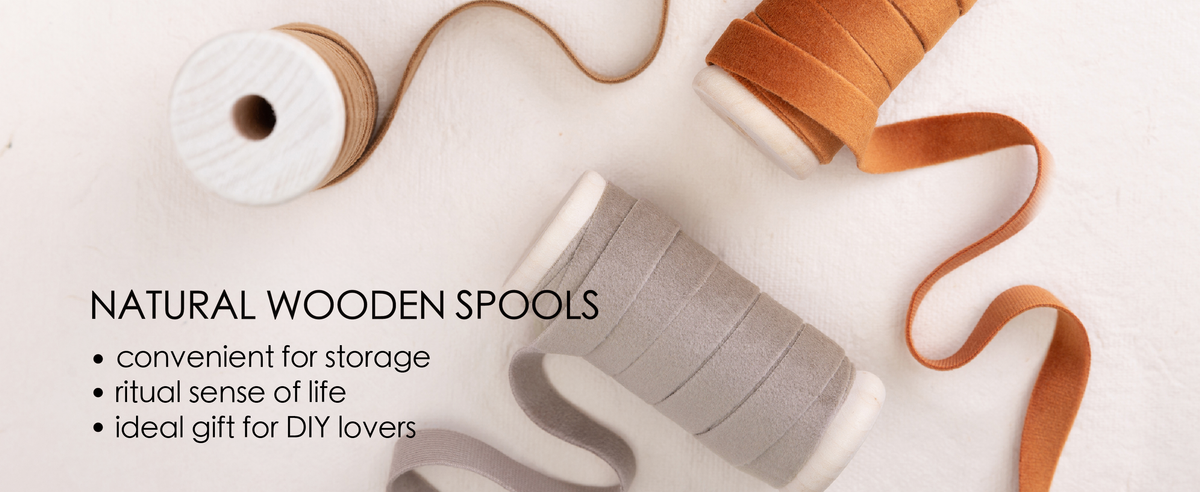 Orange, gray, and tan velvet ribbons wound on natural wooden spools over cream fabric.