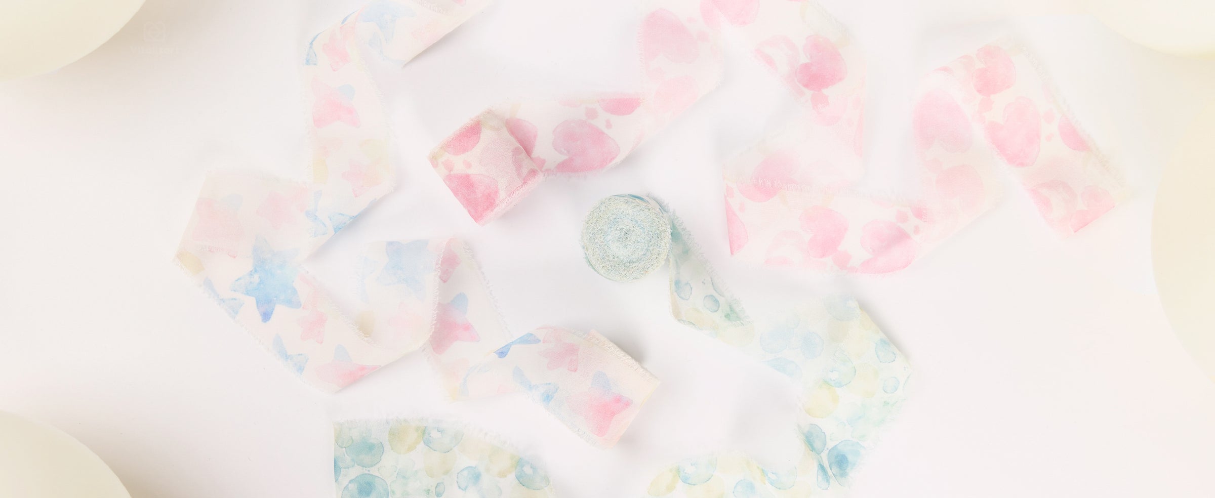 Frayed chiffon ribbons with pastel pink spots, blue stars, and aqua circles arranged beside cream balloons