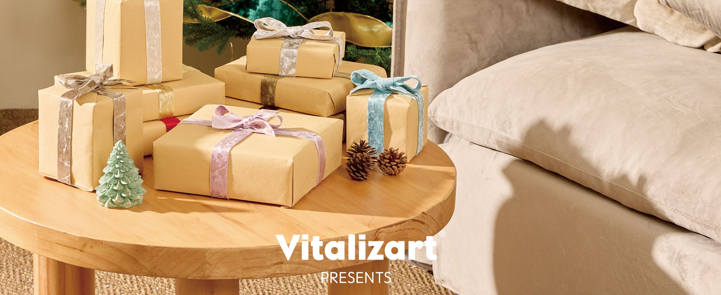 Kraft-paper Christmas gifts tied with velvet ribbons beside a decorated tree and beige armchair