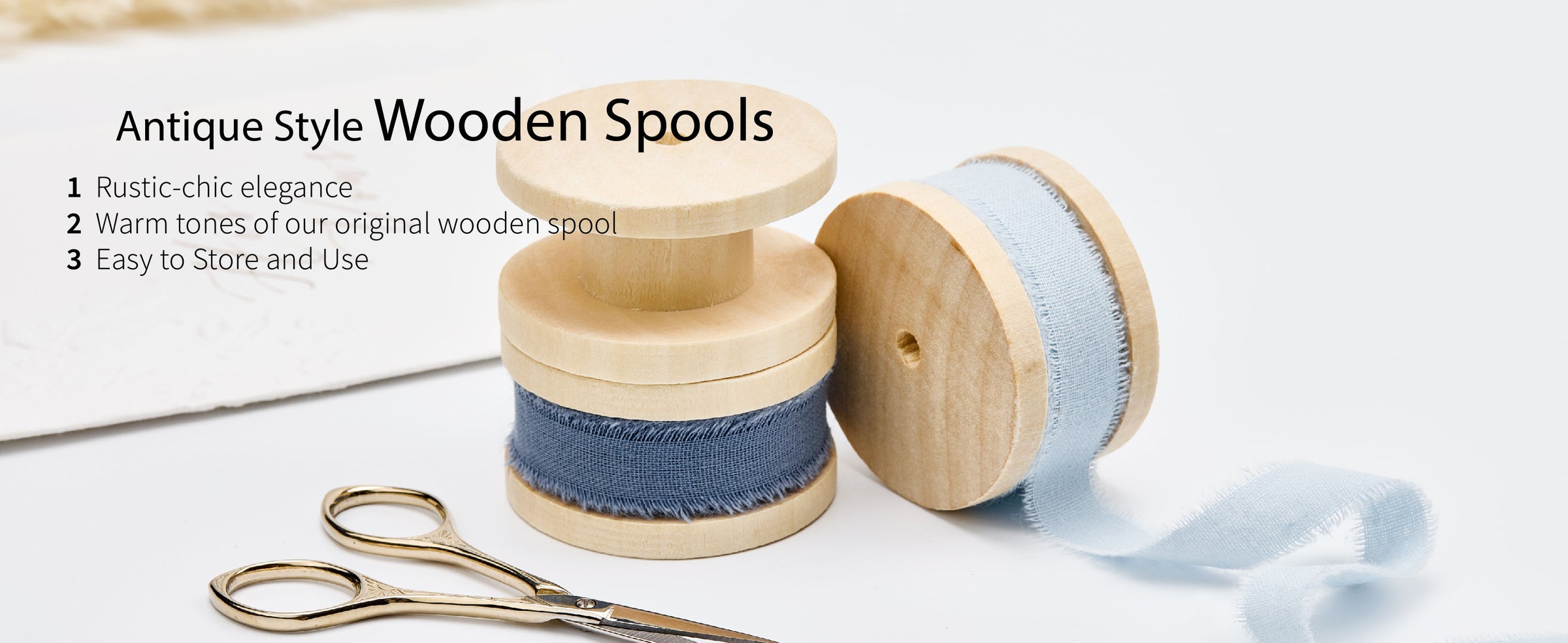 Medium and light blue frayed cotton ribbon on pale wooden spools beside small gold craft scissors