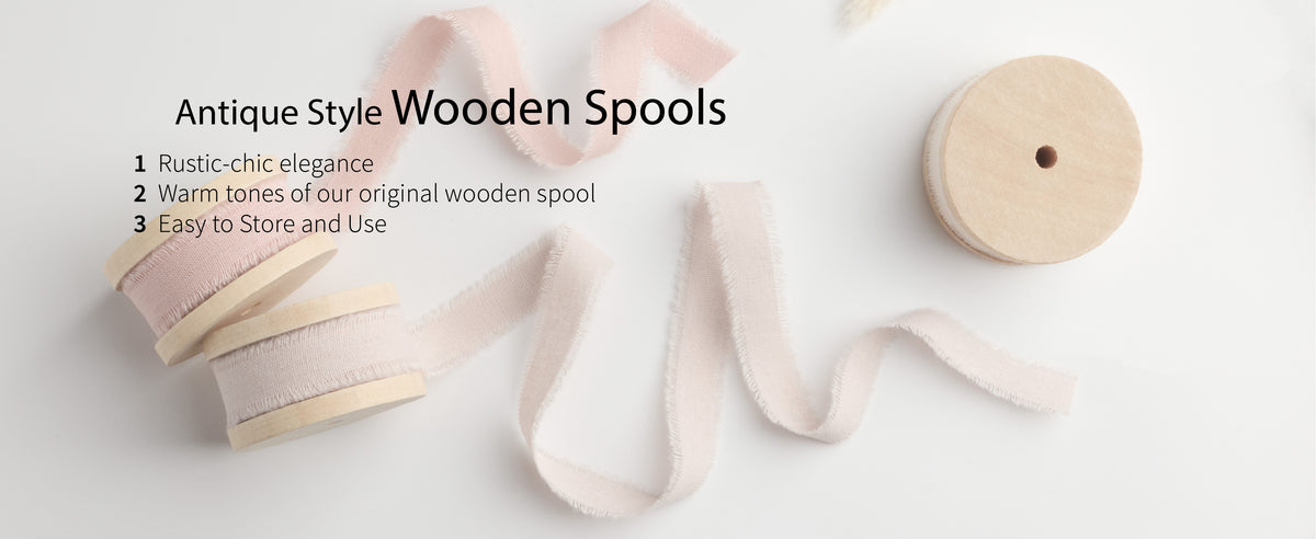Pale pink fringed cotton ribbon unwinds from two light wooden spools on a white surface.