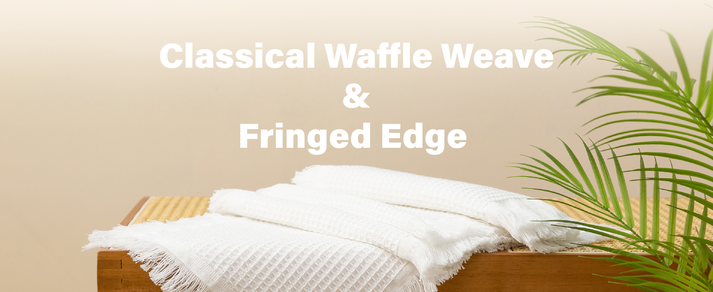 Stacked white waffle-weave table runners with fringed edges on a wooden bench beside palm leaves