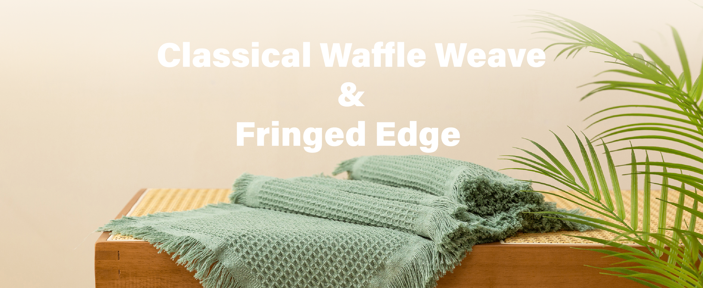 Folded dusty green waffle-weave table runners with fringed edges stacked on a wooden bench