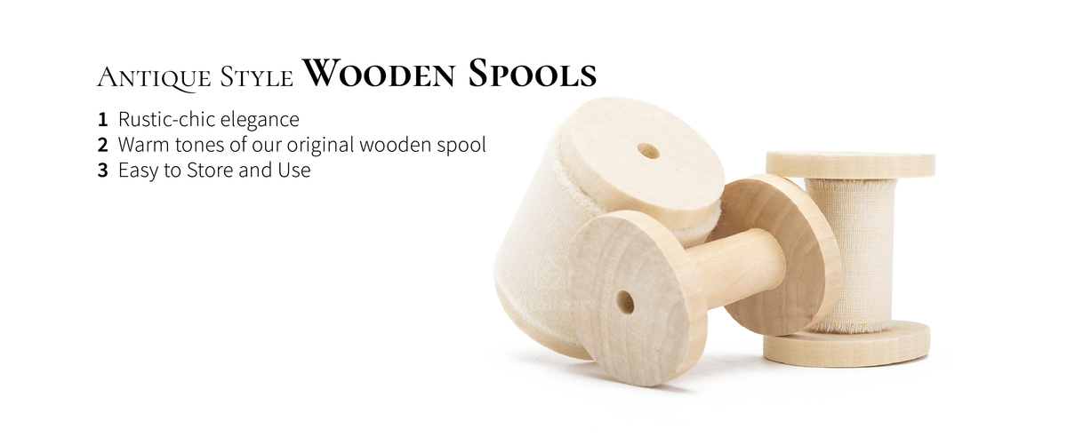 Cream-white fringed cotton ribbon on pale antique-style wooden spools, with one empty spool in front.