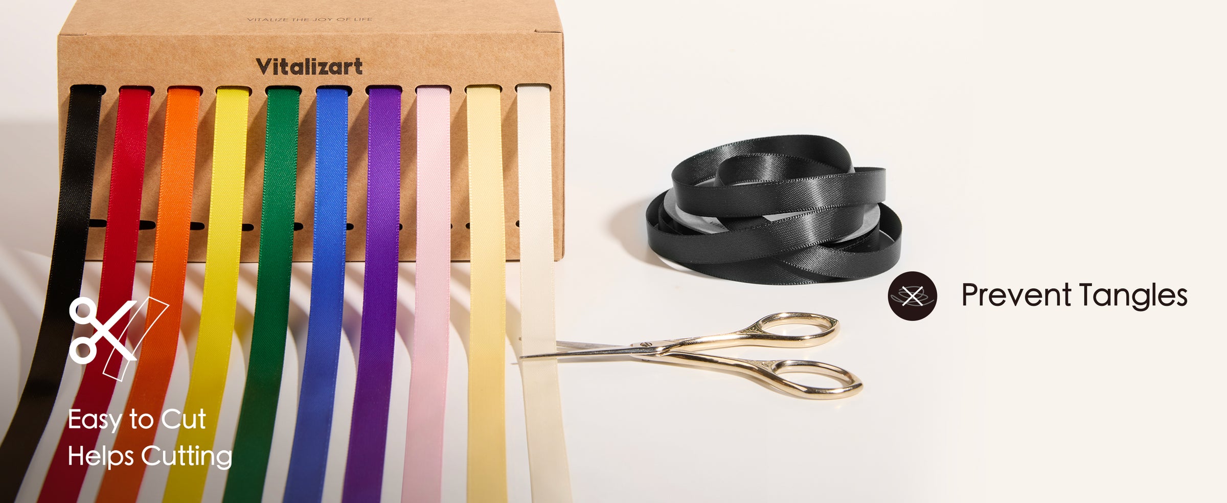 Rainbow satin ribbons feed from a dispenser box beside scissors and a loose black ribbon coil