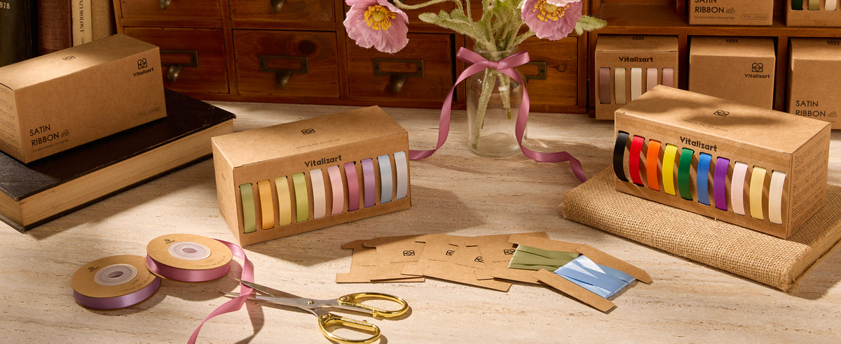 Kraft dispenser with ten colorful satin ribbons beside ribbon cards, scissors, and a flower vase.