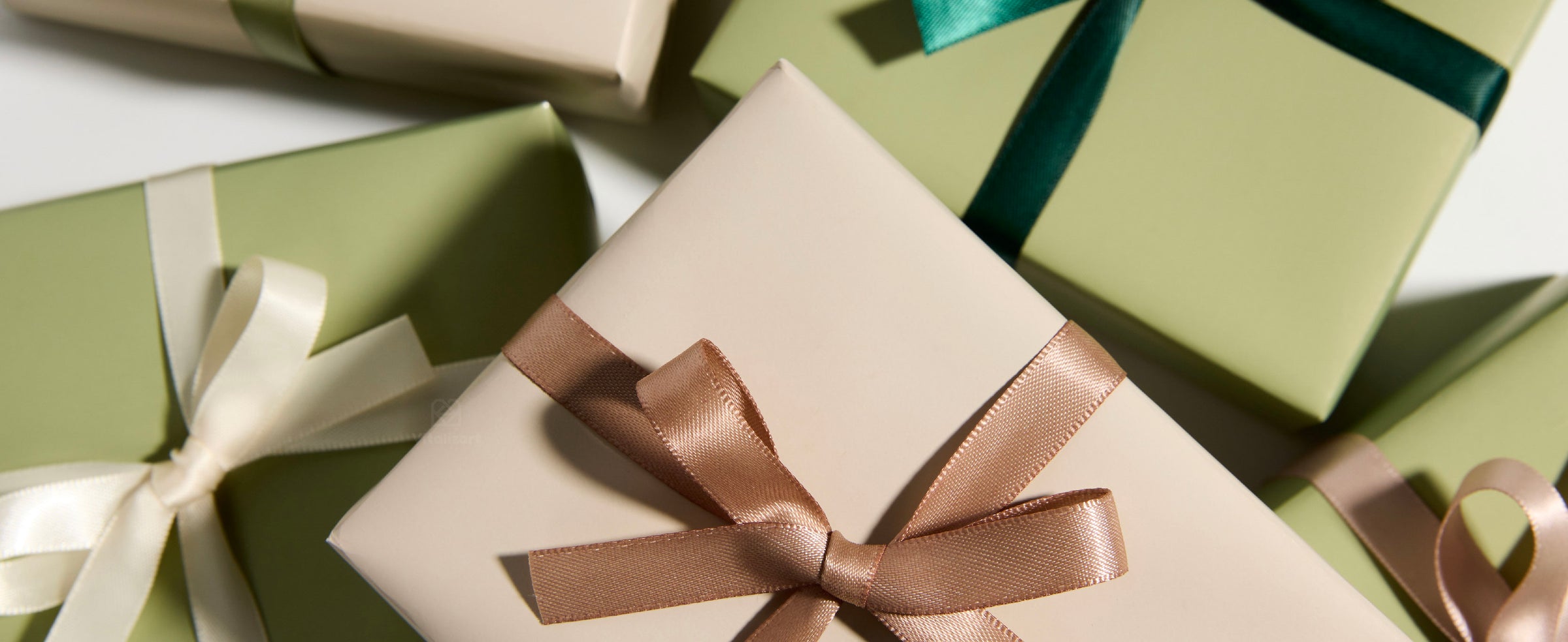 Cream and pale green gift boxes tied with glossy teal, sage, ivory, and blush satin bows.