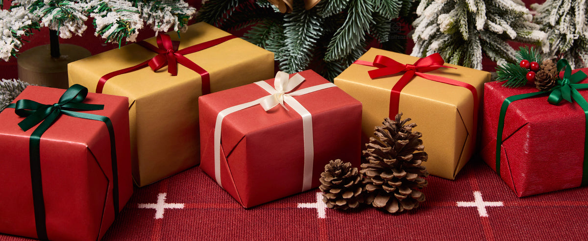 Christmas gifts tied with red, cream, green, and teal satin ribbons beneath snowy evergreen branches.