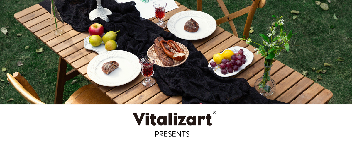 Black cheesecloth table runner draped across an outdoor table set with fruit, bread, and drinks.