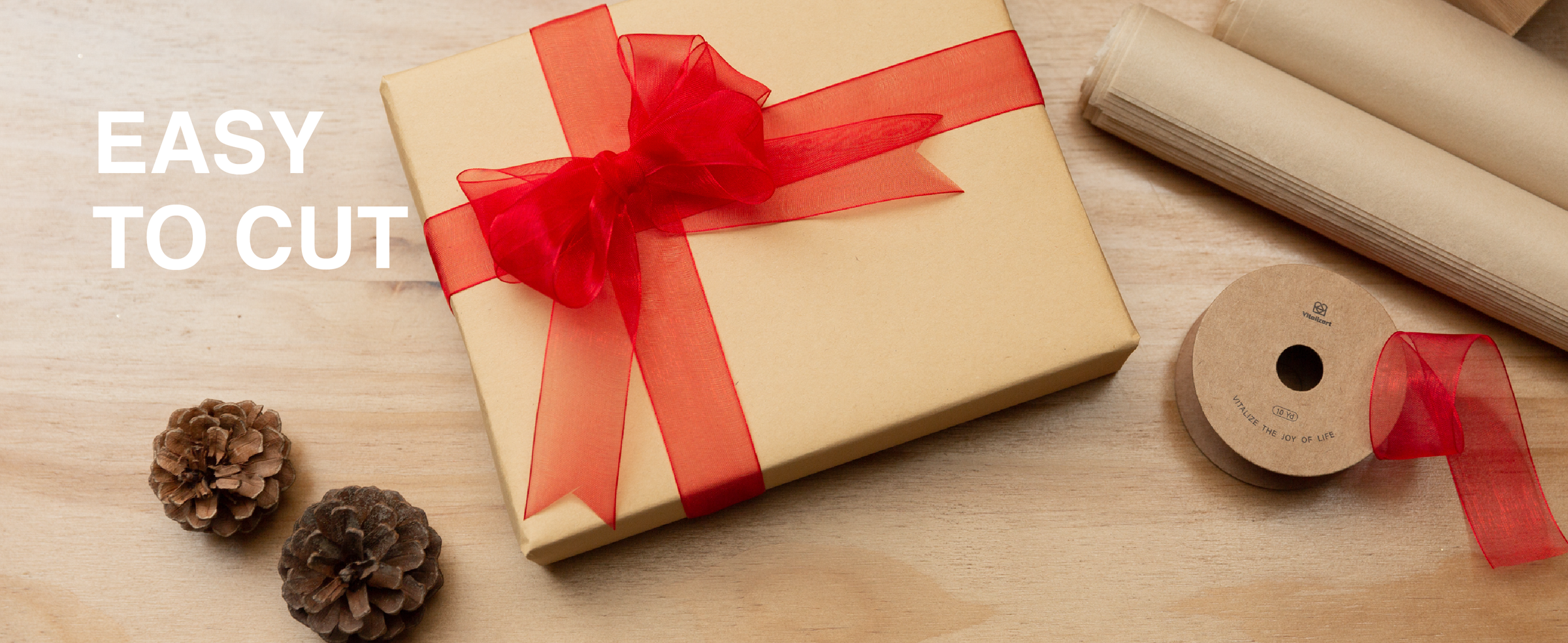 Red sheer ribbon tied in a bow around a kraft gift box beside scissors and a spool
