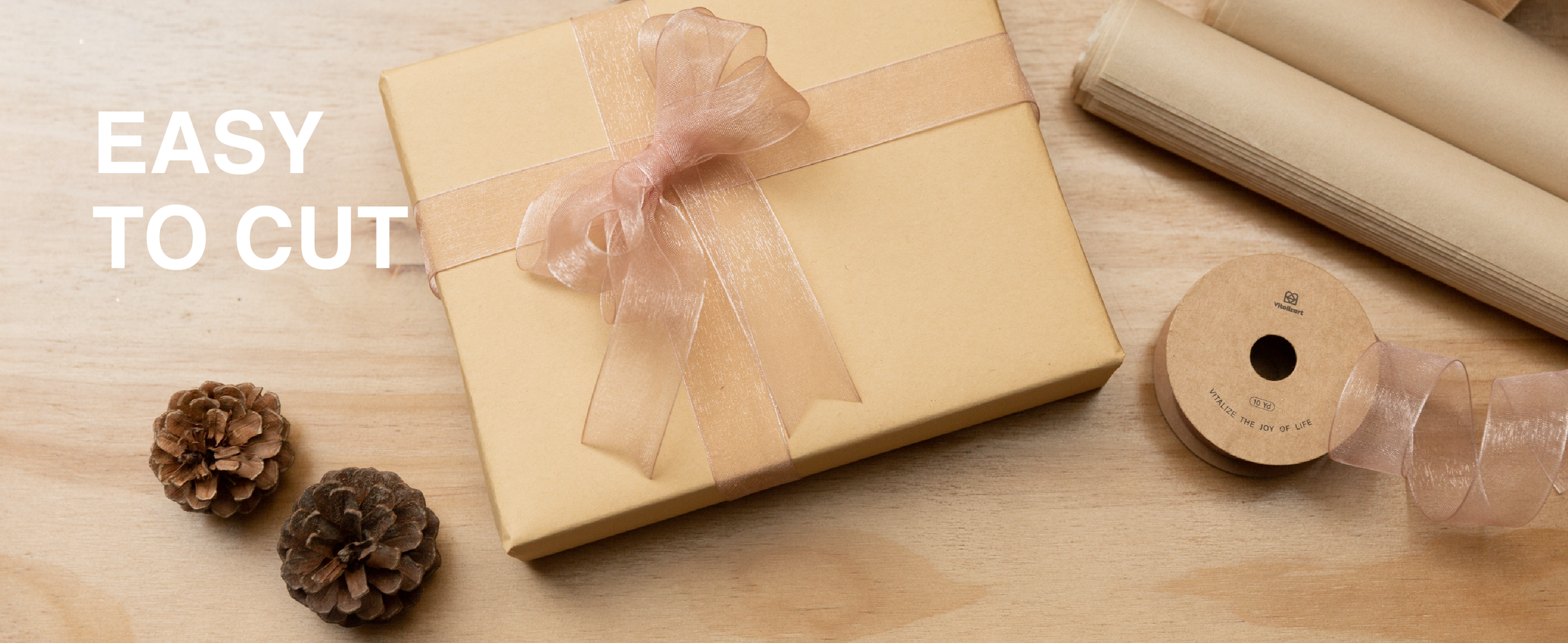 Rose-pink sheer organza ribbon tied around a kraft gift box beside scissors and a matching spool.