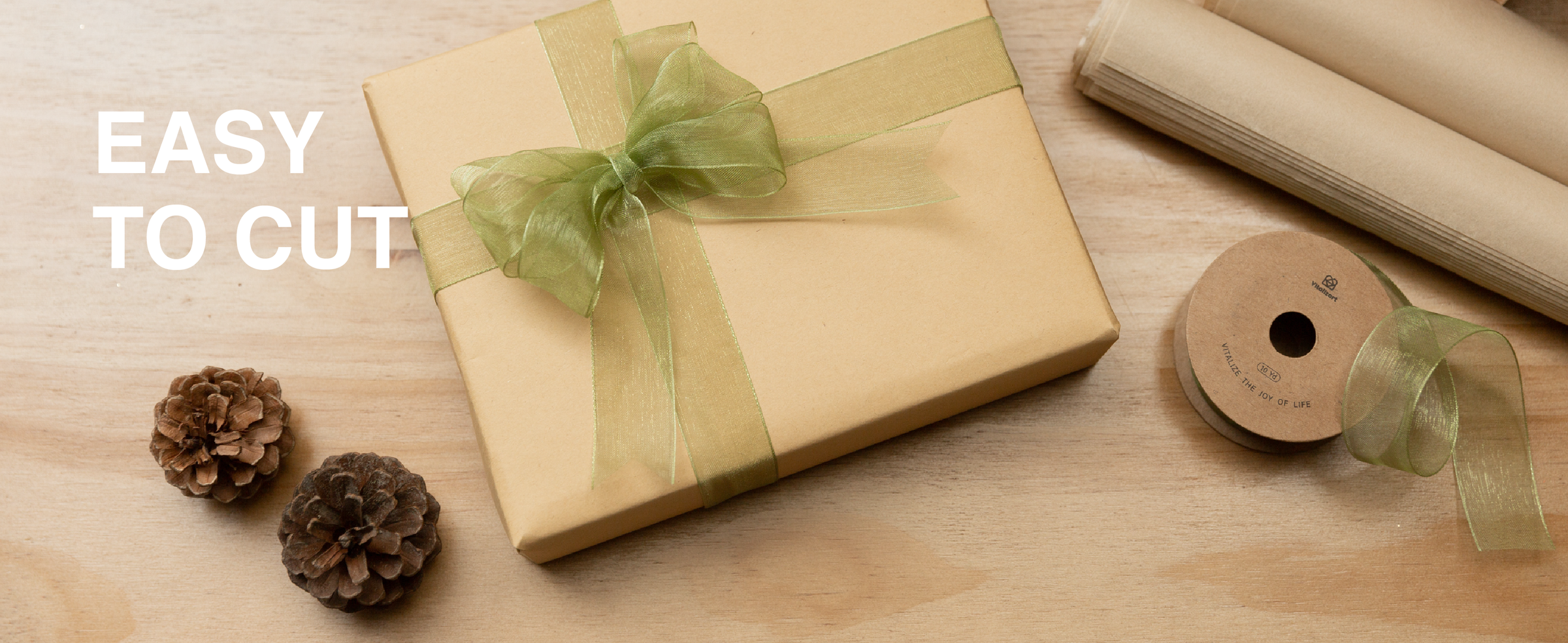 Sage green sheer organza ribbon tied around a kraft gift box beside scissors and a spool.