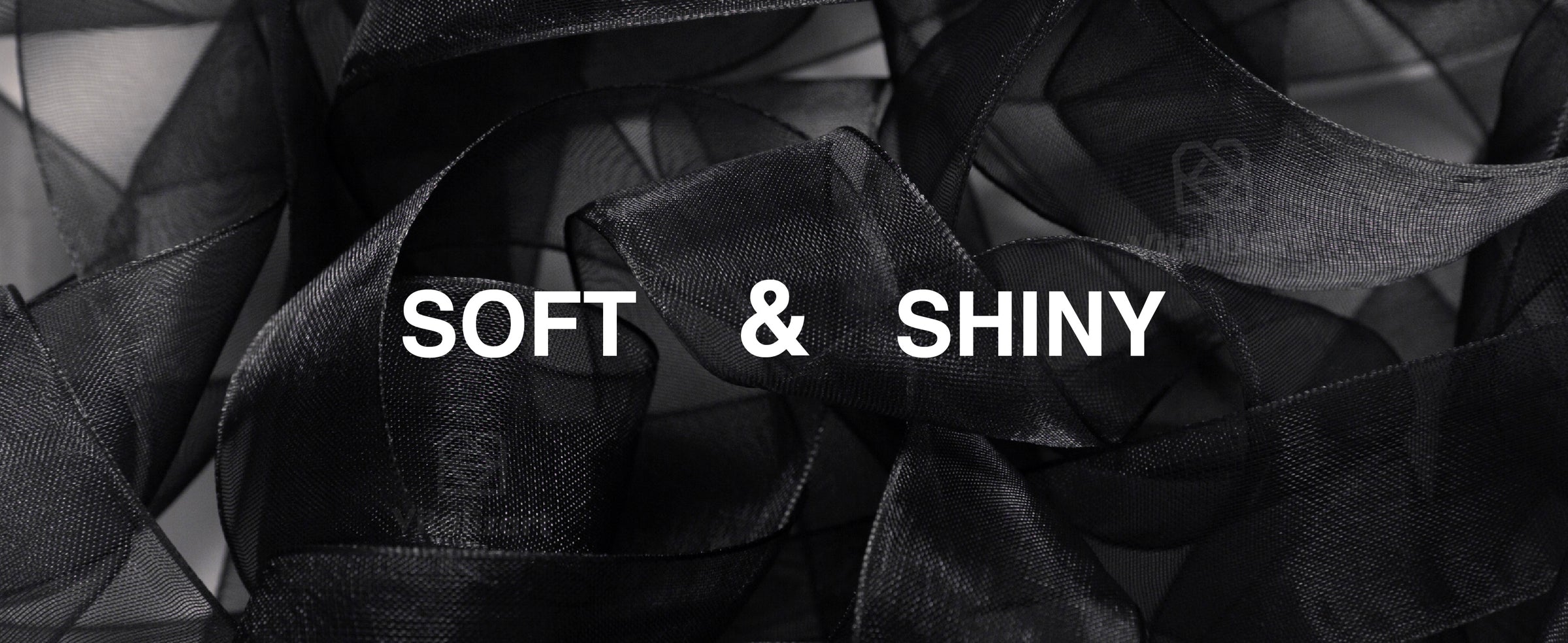 Close-up of soft, shiny black organza ribbon showing its translucent weave and finished edges.