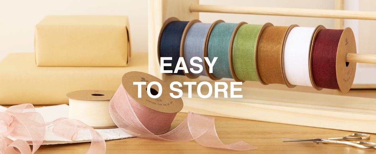 Mixed-color sheer organza ribbon rolls stored on a wooden rack with pink ribbon unspooled