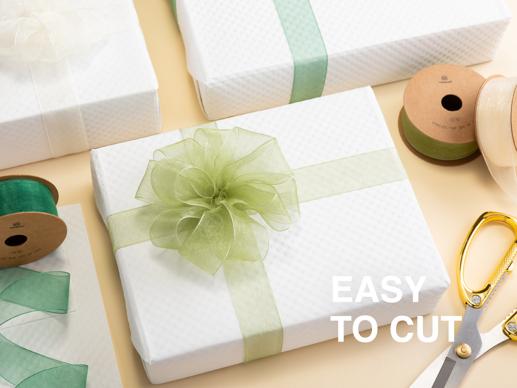 Pale green organza ribbon tied in a large bow around a white gift box beside a ribbon spool