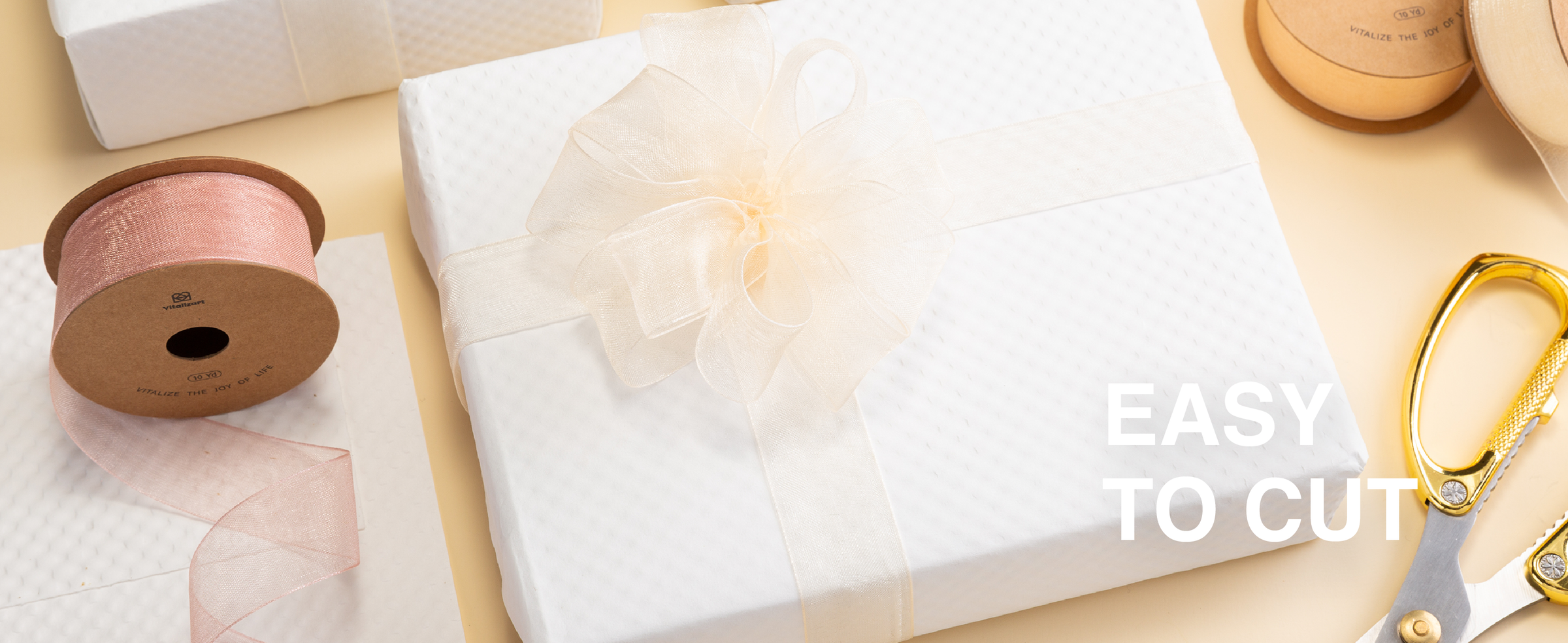 Cream organza ribbon tied into a large bow on a white gift box, with spools and scissors nearby.