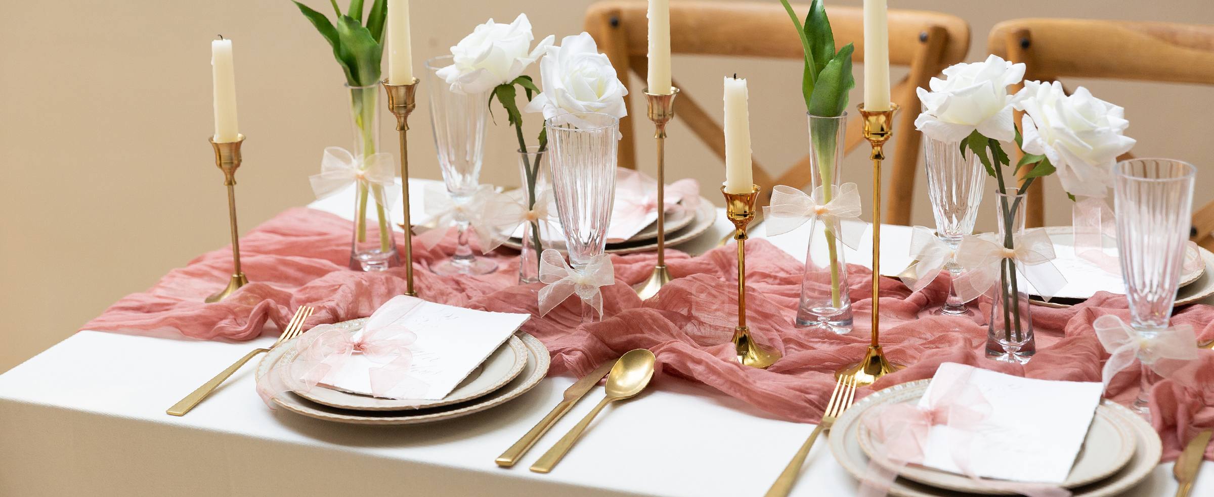 Cream organza ribbon bows decorate glasses, vases, and place settings on a pink formal table.