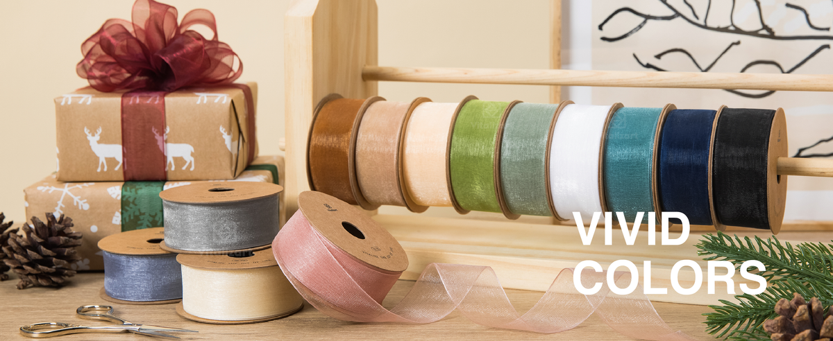 Colorful organza ribbon spools displayed on a wooden rack with loose blush ribbon in front.