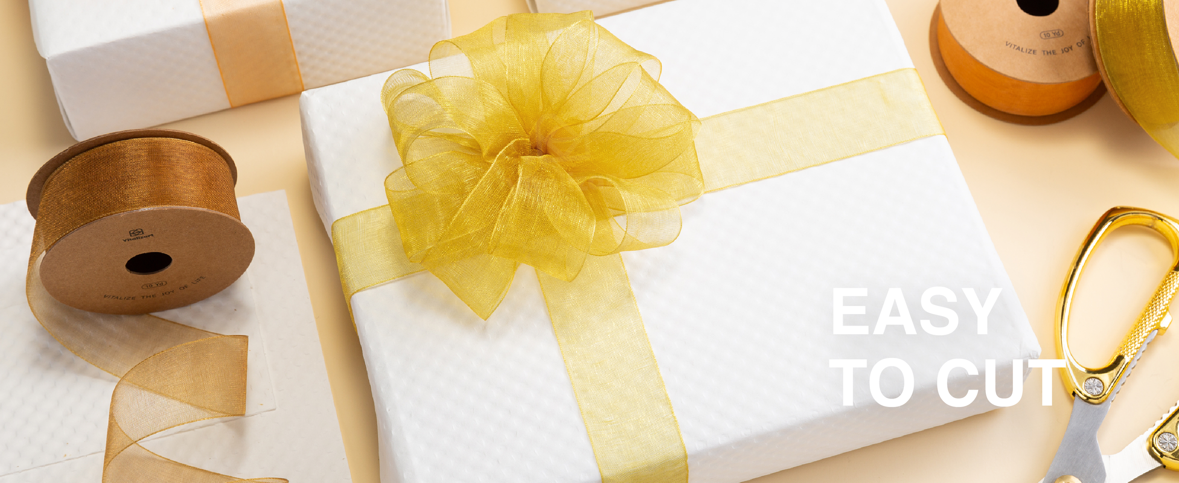 Bright gold sheer organza ribbon tied in a full bow around a white gift box beside scissors