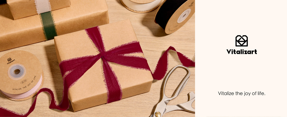 Deep red frayed chiffon ribbon tied around a kraft gift box beside spools and scissors