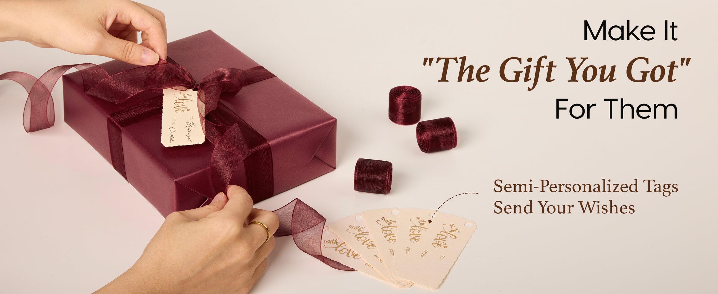Hands tie burgundy organza ribbon and a writable cream tag onto a pearlescent wrapped gift