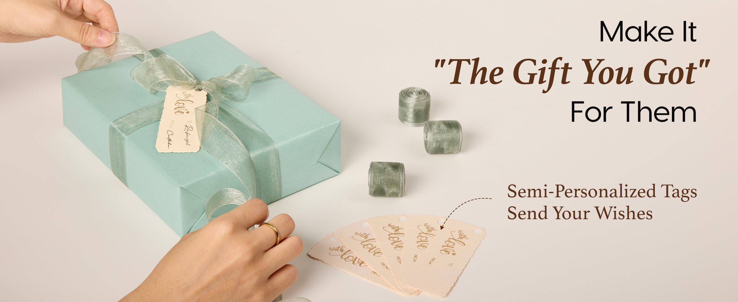 Hands tie pale-green organza ribbon and a writable cream tag onto a sage pearlescent gift