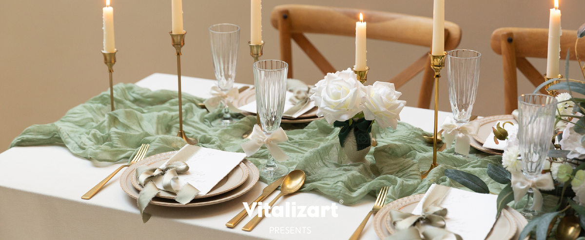 Cream satin ribbon bows accent glasses on a sage-green table set with white roses and gold candlesticks.