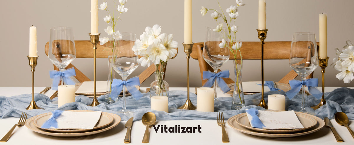 Dusty blue chiffon ribbon bows decorate wine glasses on an elegant table with flowers and candles.