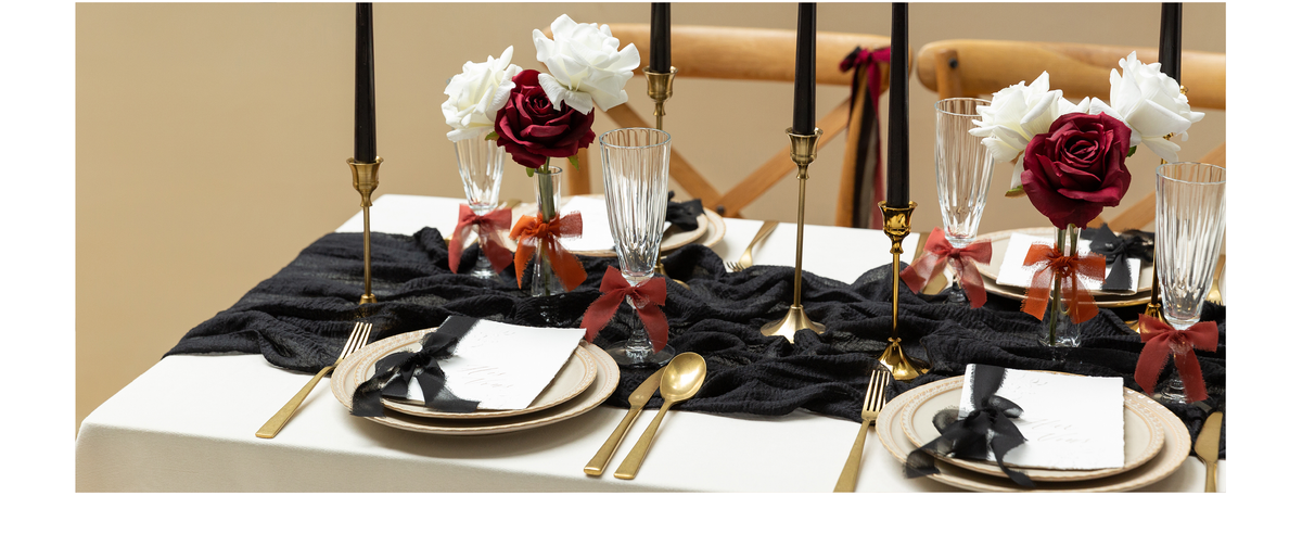 Black, rust, and burgundy chiffon ribbons decorate cards, glasses, and rose vases on a formal table